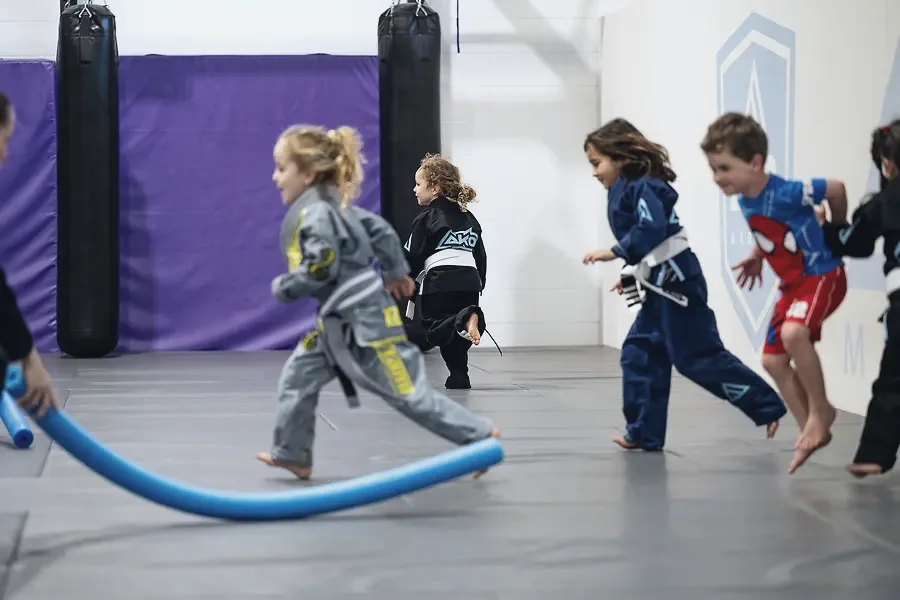 Young kids running with a pool noodle in a Jellyfish class at Ako Martial Arts