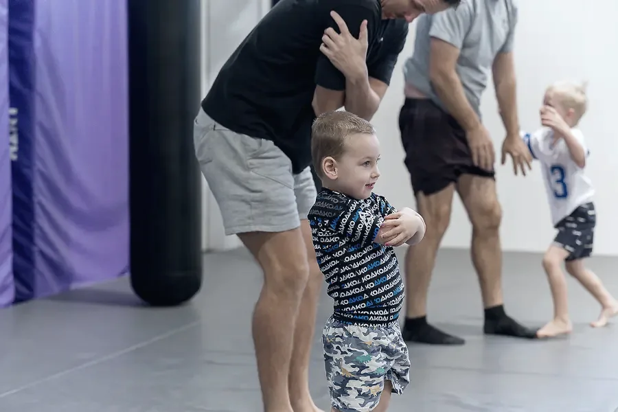 A coach helping a toddler on the mats in a Guppies class
