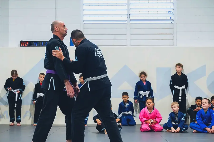 Two coaches demonstrating a technique to a group of seated kids