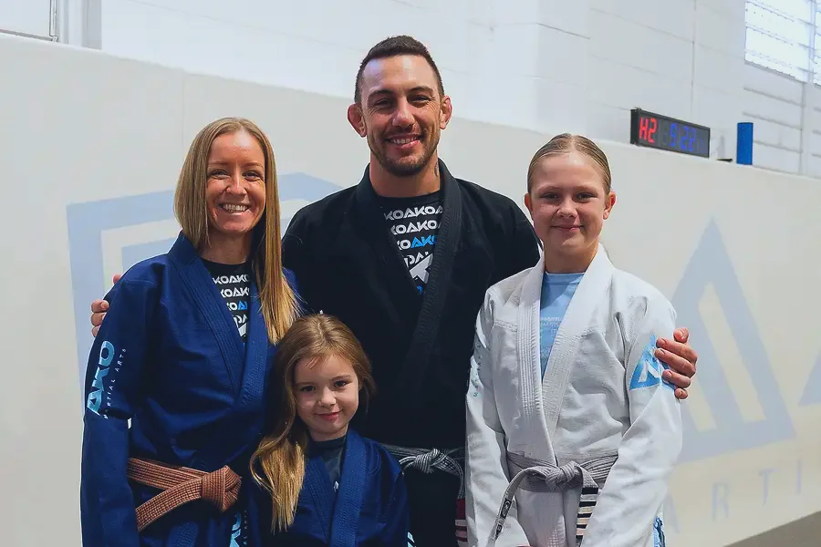 A coach smiling with two young students on grading day