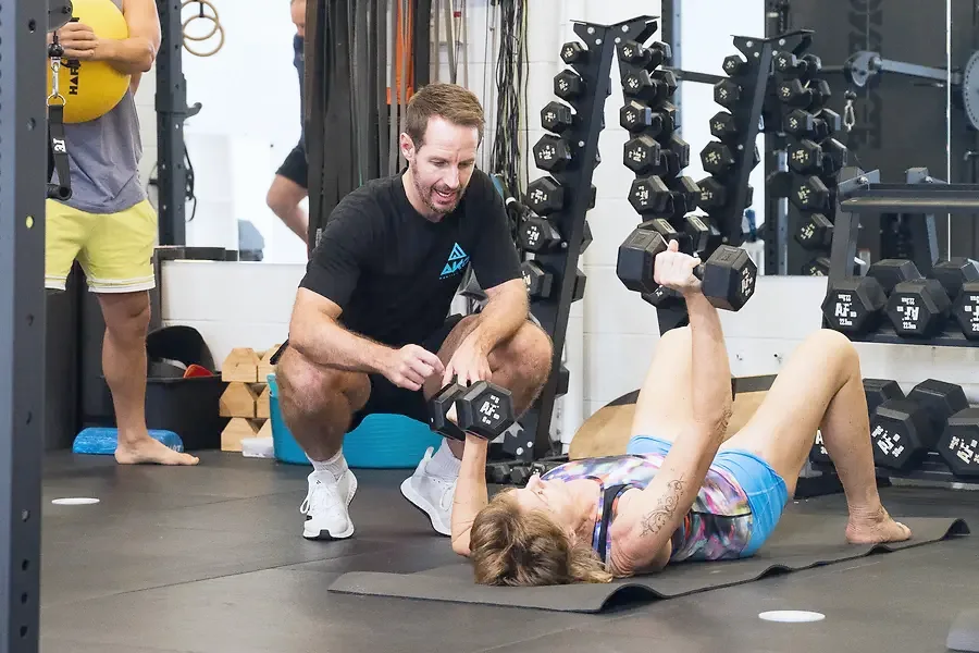 A coach guiding a member through a dumbbell press while others train